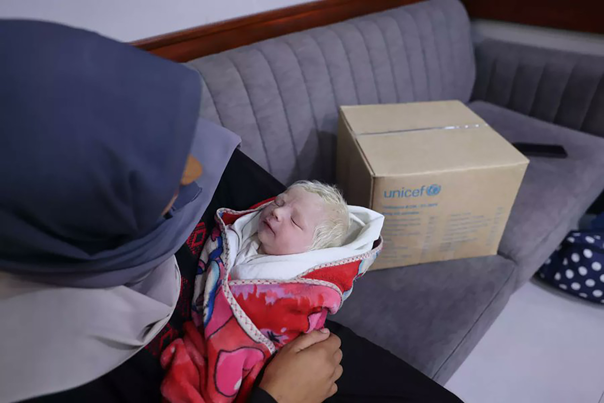 A woman holds her baby with a UNICEF box of supplies in the background.